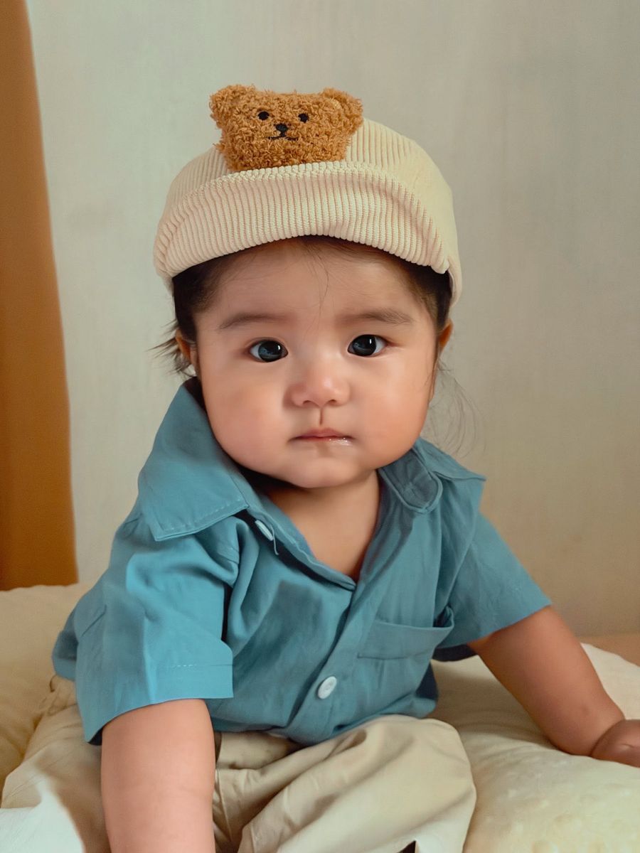 Baby wearing a teddy bear cap and a teal shirt