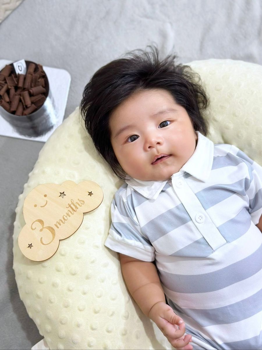 Three-month-old baby with a full head of dark hair on a cream pillow